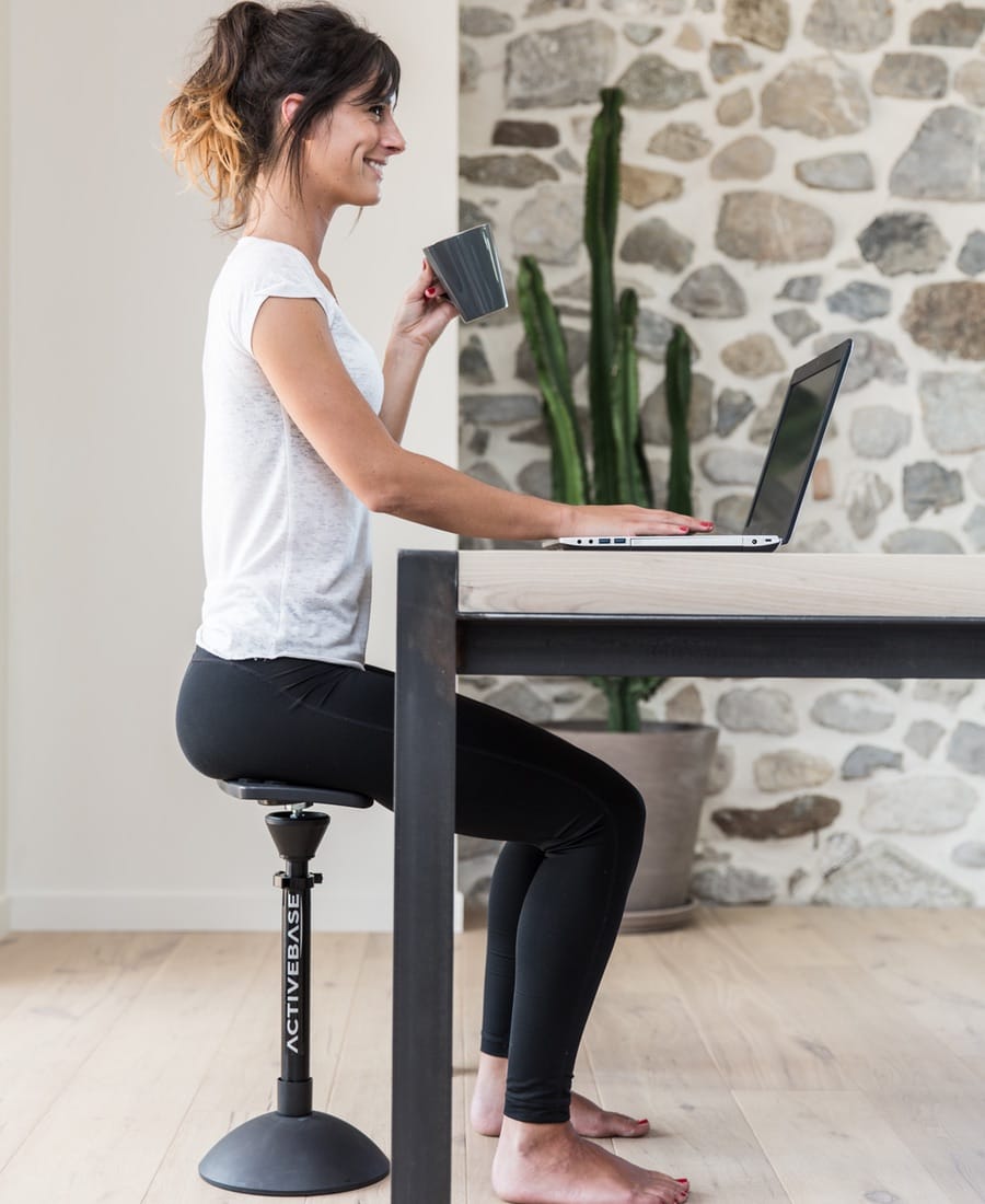 A woman sitting on the ergonomic ActiveBase seat is using her laptop, encouraging active sitting.